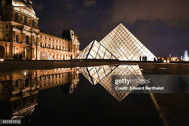 The Louvre museum, including the Louvre Pyramid made of glass and metal, reflects into a water puddle on a rainy summer day, during night time, on...