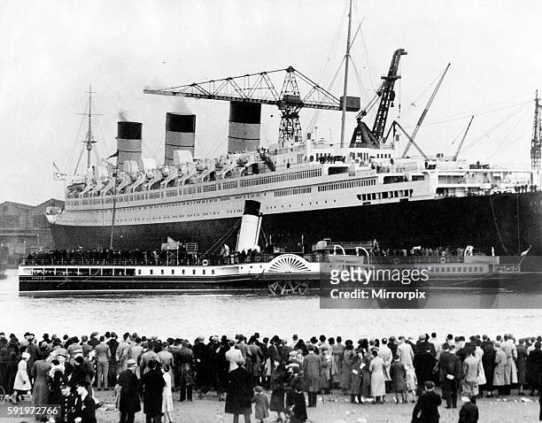 The Cunard White Star ocean liner Queen Mary in the Clyde. Crowds on shore as the Clyde Paddle steamer Eagle III passing the Queen Mary laden with...
