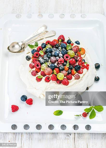 homemade pavlova cake with fresh garden berries served with silver spoons on white baking tray over white painted wooden background - gooseberry cake stock pictures, royalty-free photos & images