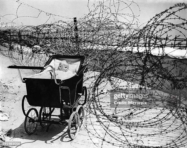 Home front. Baby enjoys the sea air as best she can at Eastbourne in Sussex, on the south coast of England, June 1941. The beach has been barricaded...