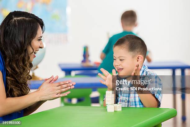 child with down syndrome clapping, playing with blocks in classroom - mental disability stock pictures, royalty-free photos & images