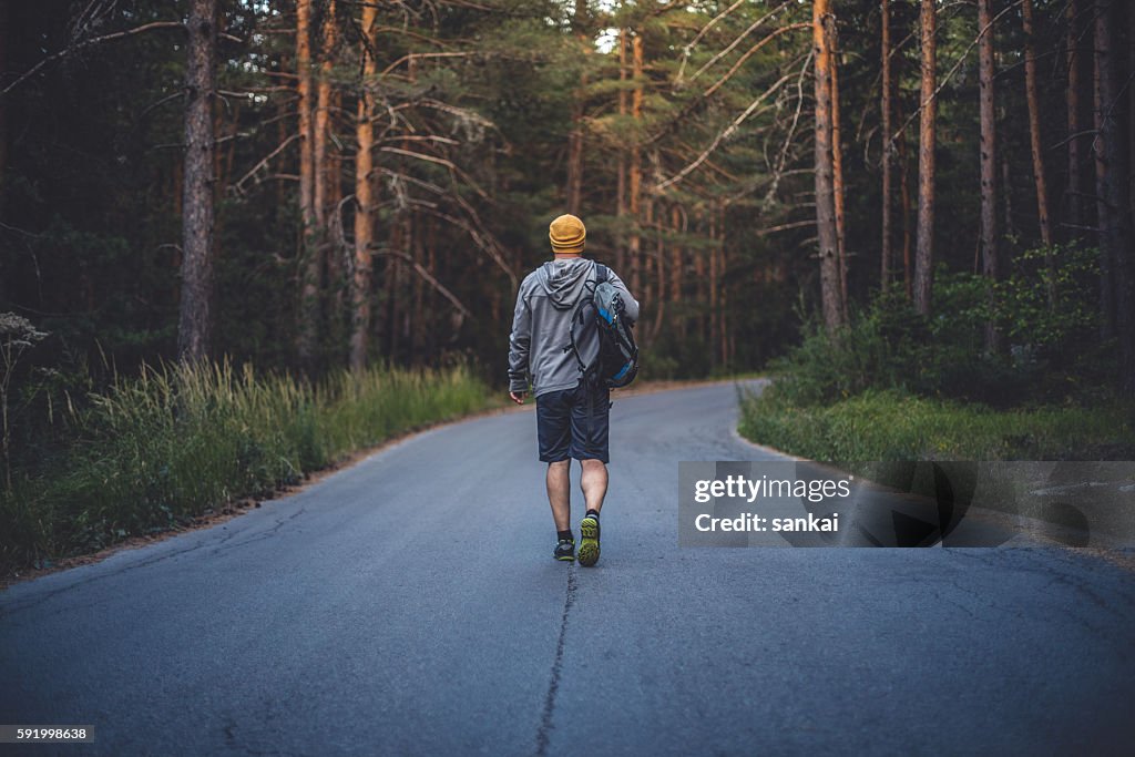 Viajante masculino com mochila caminha para a frente pela estrada