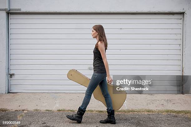 caucasian woman carrying guitar case on sidewalk - guitar case fotografías e imágenes de stock