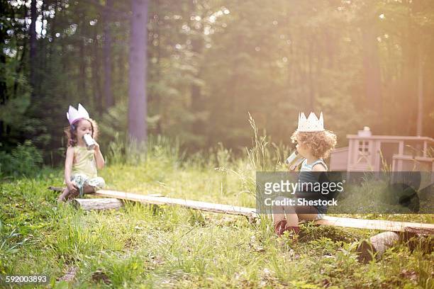 girls playing telephone on wooden log in garden - answering stock-fotos und bilder