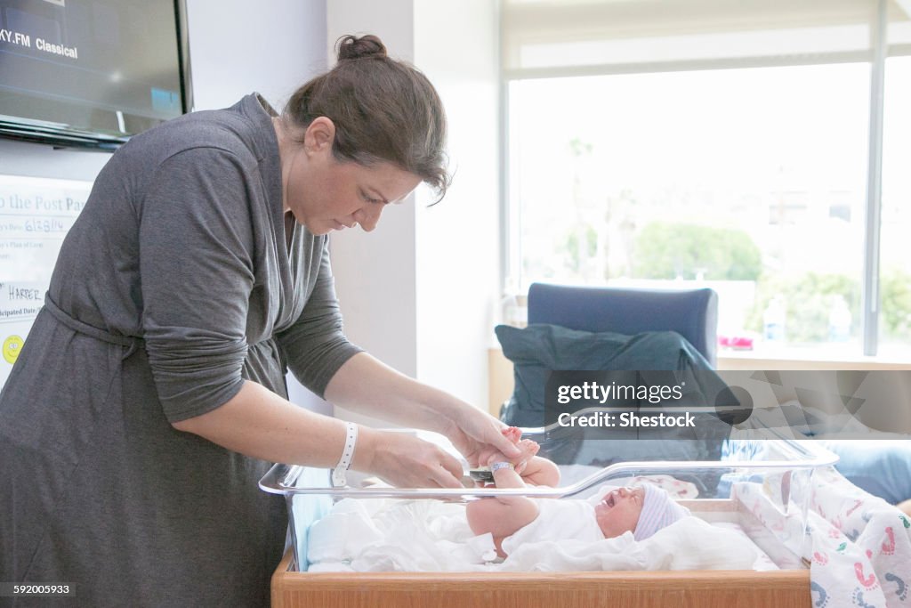 Caucasian mother changing newborn daughter in hospital crib