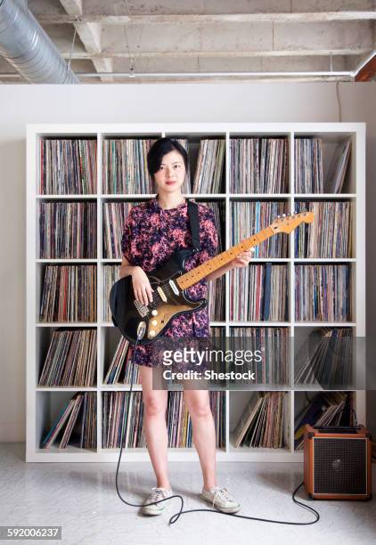taiwanese woman playing electric guitar near record collection - verstärker stock-fotos und bilder