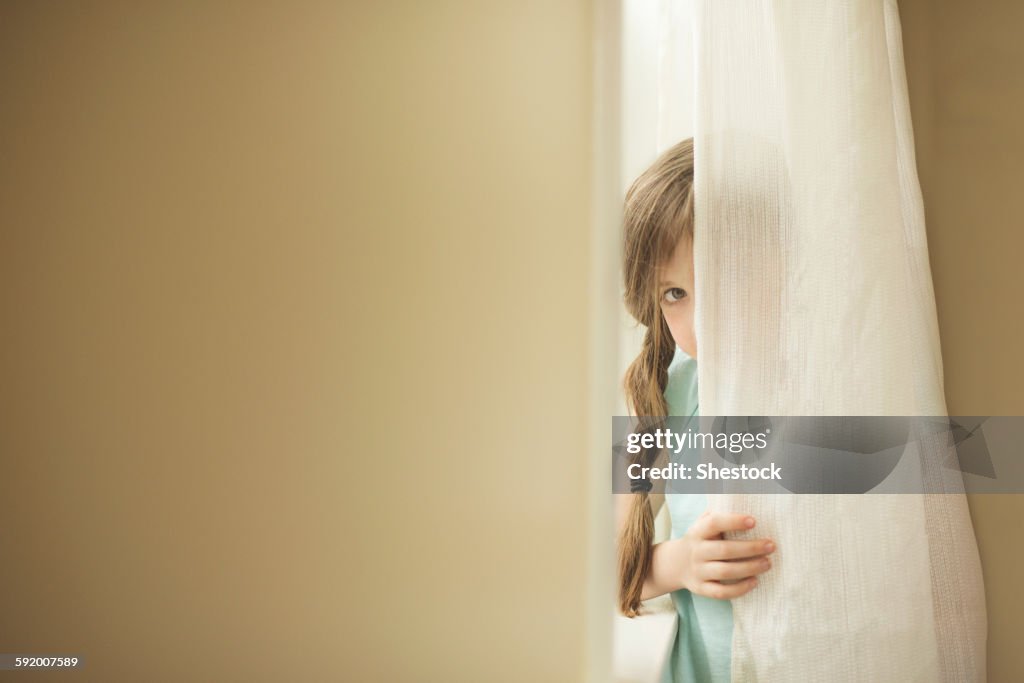 Shy Caucasian girl peeking around curtain