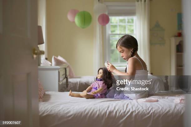 caucasian girl brushing hair of doll on bed - american girl doll stock pictures, royalty-free photos & images