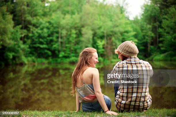 rear view of couple sitting near lake - young love stock-fotos und bilder