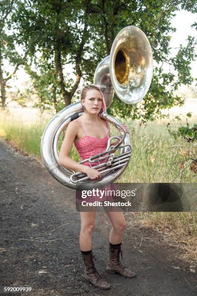 caucasian musician carrying tuba on dirt path - tube foto e immagini stock