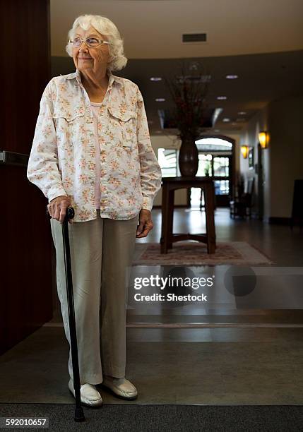 older caucasian woman standing with cane in retirement home - spazierstock stock-fotos und bilder