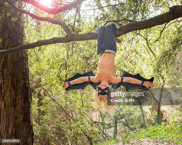 young boy dressed as a bat, hanging from tree branch - crazy youngster stock pictures, royalty-free photos & images