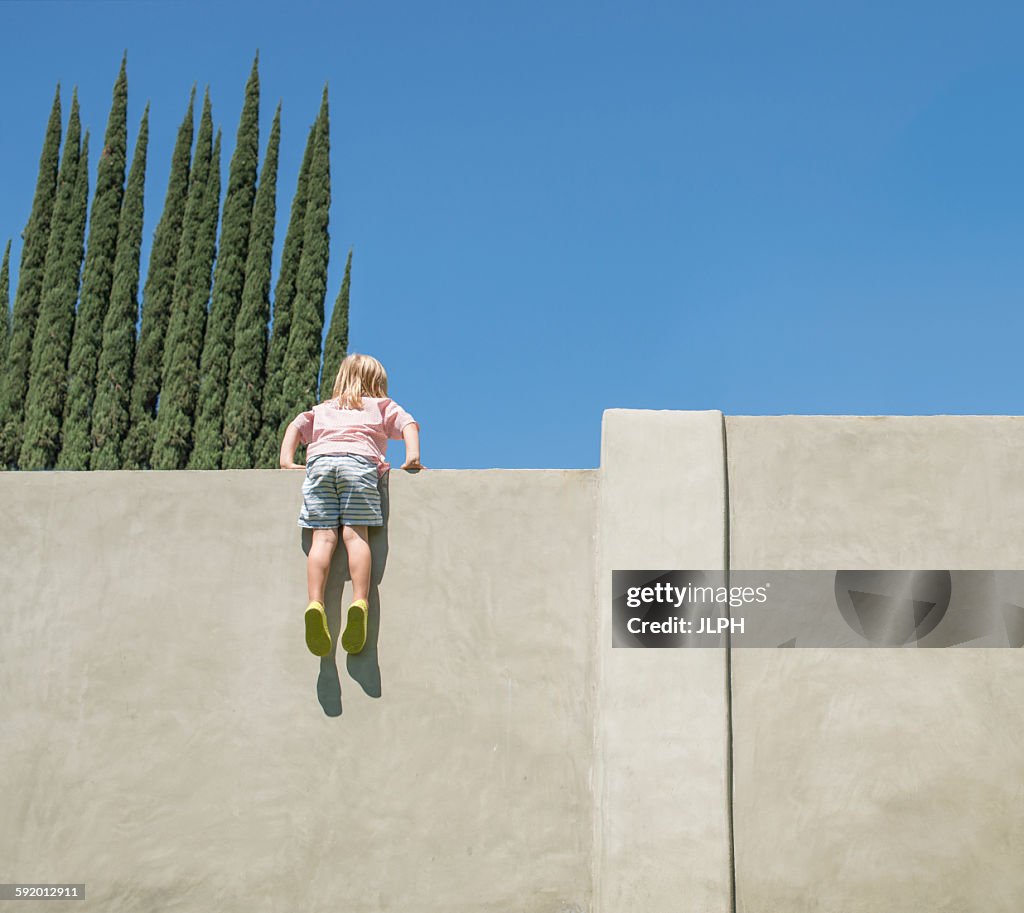 Young boy looking over tall wall, feet dangling, rear view