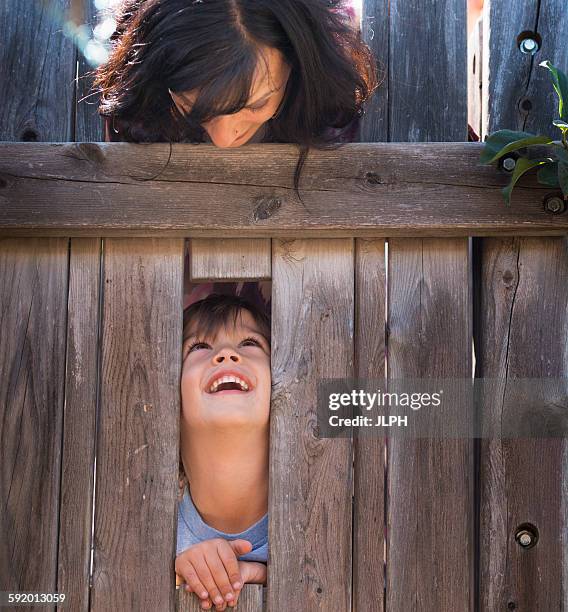 mother looking over at son, through hole in fence - ergens overheen kijken stockfoto's en -beelden