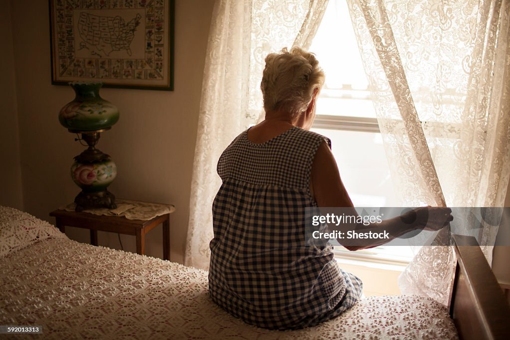 Pensive older woman looking out bedroom window