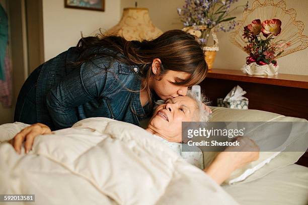 Granddaughter kissing forehead of grandmother in bed