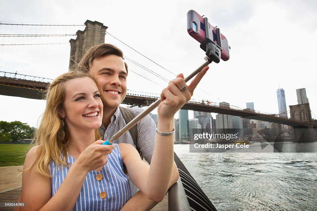 Caucasian couple taking selfie with cell phone under Brooklyn Bridge, Brooklyn, New York, United States