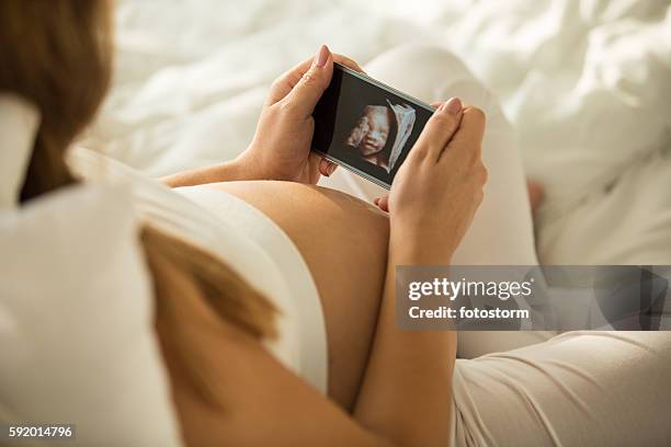 pregnant woman looking at 3d ultrasound photo of her baby - ultrasound stockfoto's en -beelden