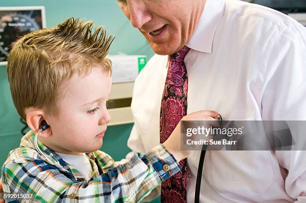 male doctor letting young boy play with stethoscope in doctors office - take care new york screening stockfoto's en -beelden