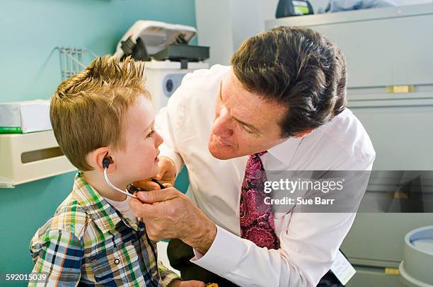 male doctor letting young boy play with stethoscope in doctors office - take care new york screening stockfoto's en -beelden