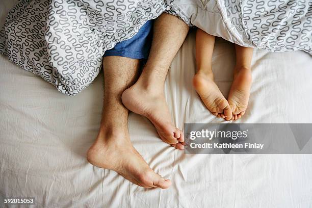 bare feet and legs of father and young son lying in bed - mens bare feet fotografías e imágenes de stock