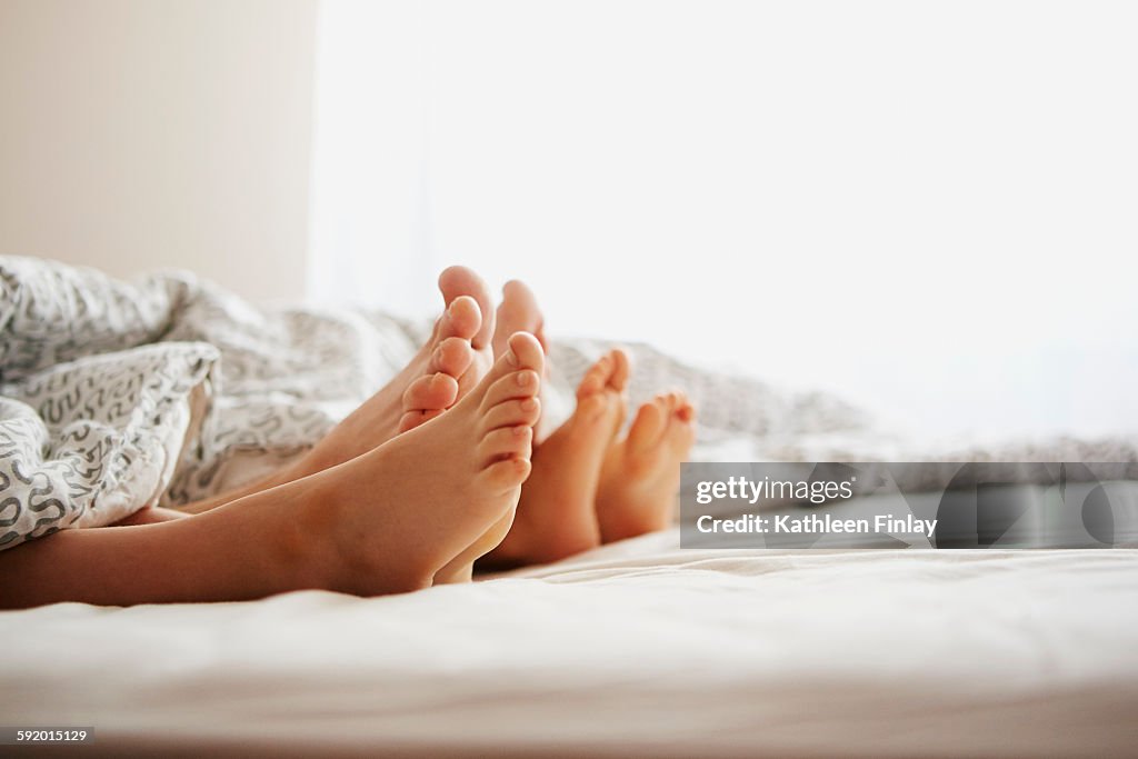 Bare feet of parents and son lying in bed