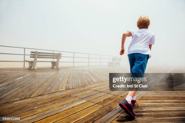 caucasian boy running on wooden boardwalk - boy running back stock pictures, royalty-free photos & images