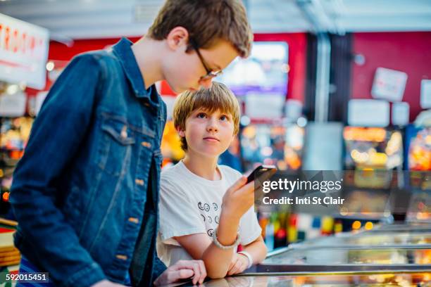 caucasian brothers using cell phone in arcade - pinball stock pictures, royalty-free photos & images