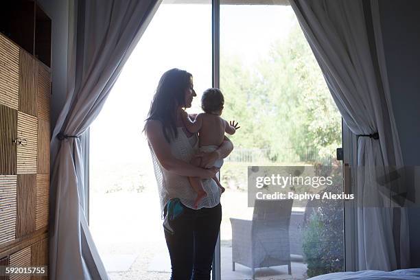 mother holding baby boy in front of patio door, looking away - santa clarita stock pictures, royalty-free photos & images