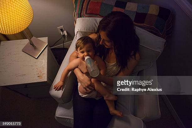 high angle view of mother in armchair feeding baby boy from baby bottle - santa clarita stock pictures, royalty-free photos & images