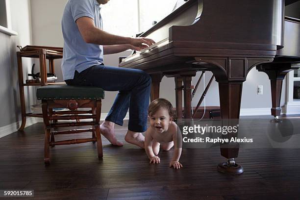 father playing piano with baby boy crawling at feet - santa clarita stock pictures, royalty-free photos & images