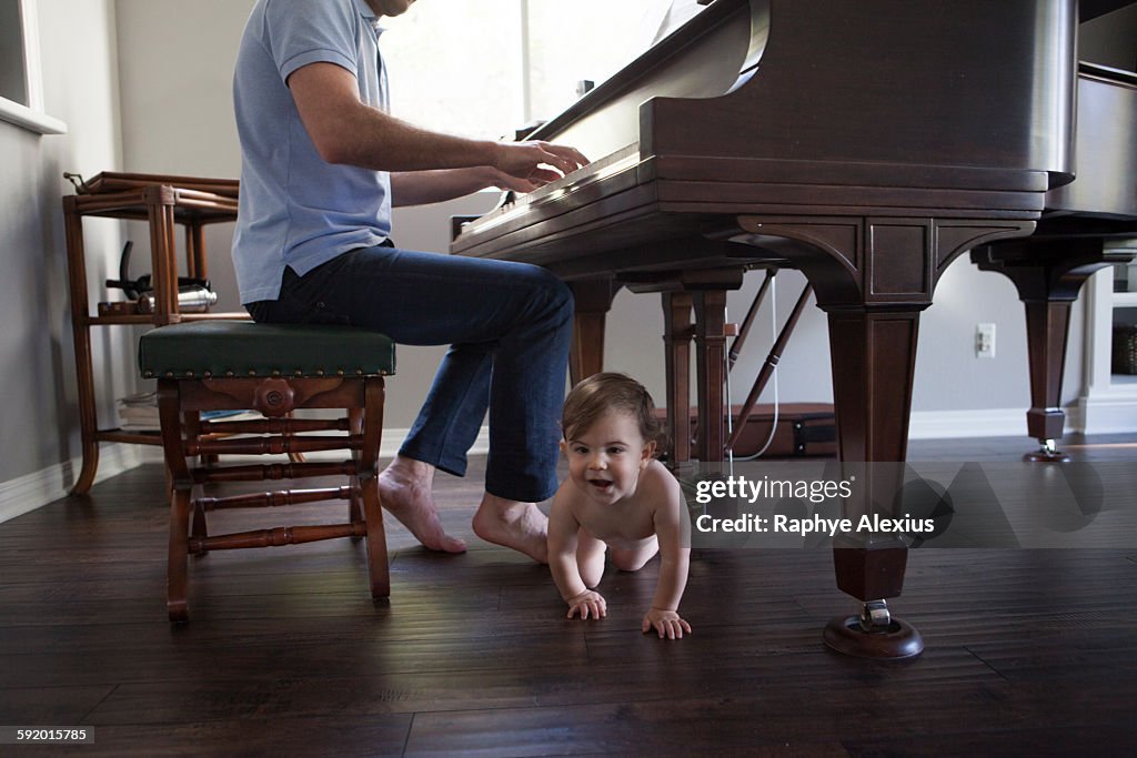 Father playing piano with baby boy crawling at feet