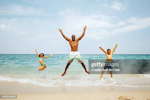 father and children jumping for joy on beach - celebration fl stock pictures, royalty-free photos & images