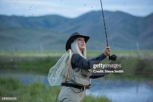 caucasian woman casting fishing line in remote lake - lenza foto e immagini stock