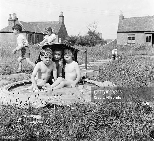 Here four year old Patricia Dunn lets the boys under her parasol to get some shade. They are left to right: Hamish McCallum, Patricia and Jack...