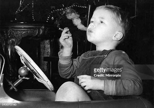 Three year old David Fellows, puffs away happily in his pedal-car, on a man-sized cigar. Mr. Fellows, who has four other children, allows David to...