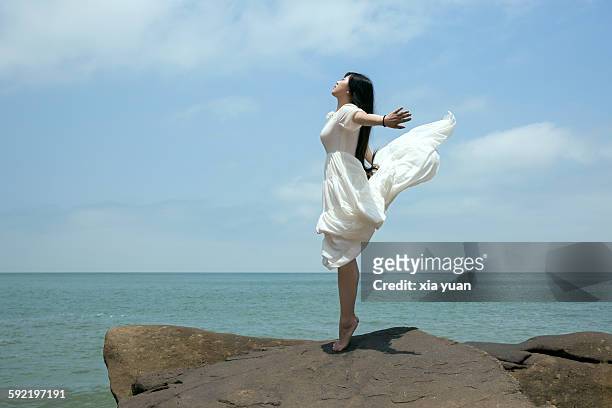 young asian woman dancing on cliff against sky - woman cliff stock pictures, royalty-free photos & images