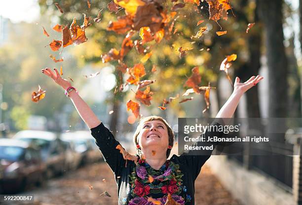 woman throwing leaves in autumn - jc bonassin stockfoto's en -beelden