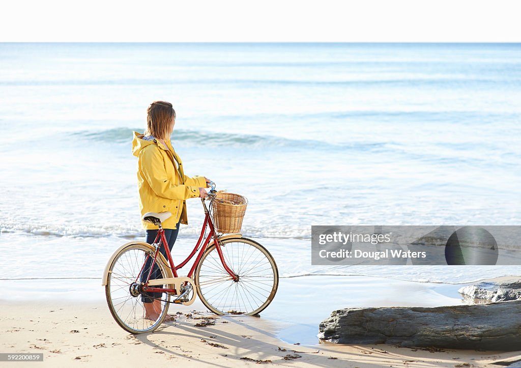 Woman with bike and yellow rain coat at beach.
