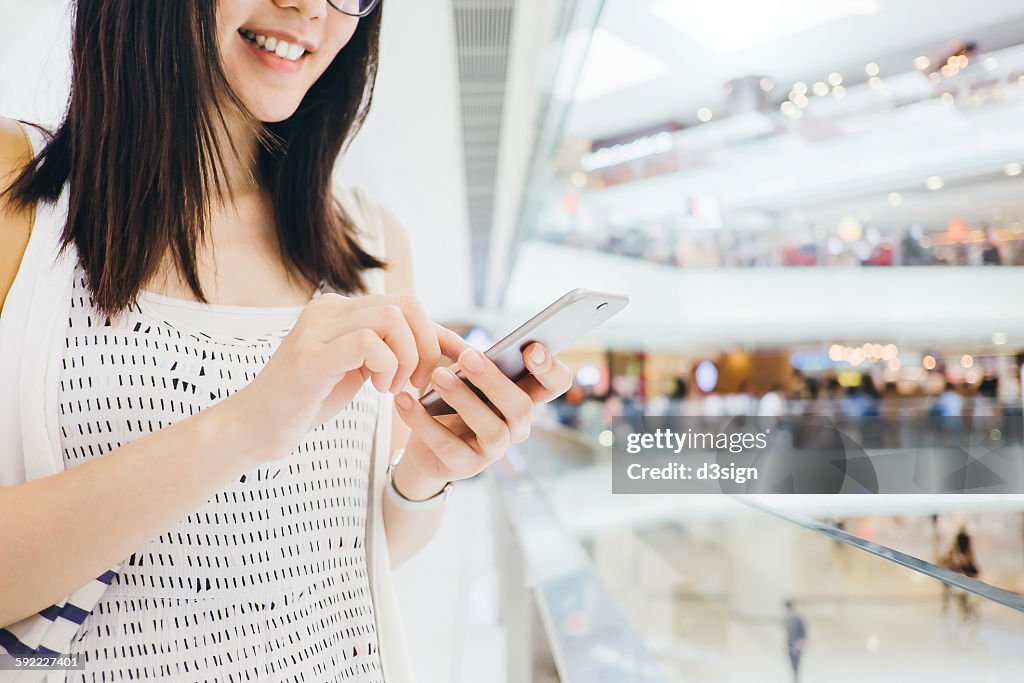 Cheerful woman using smartphone in shopping mall