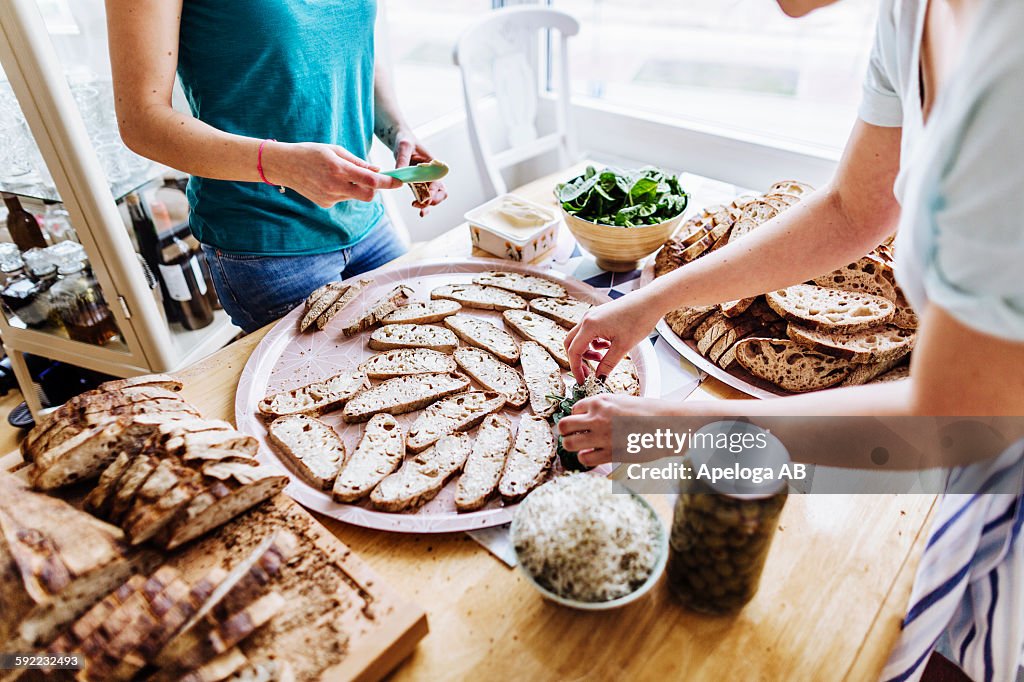 Midsection of female friends preparing open faced sandwiches at table