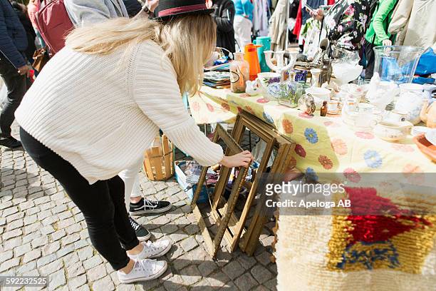 young woman looking at picture frames in flea market - rommelmarkt stockfoto's en -beelden