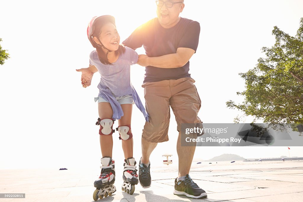 Mature man supporting daughter rollerblading at beach, Zhuhai, Guangdong, China