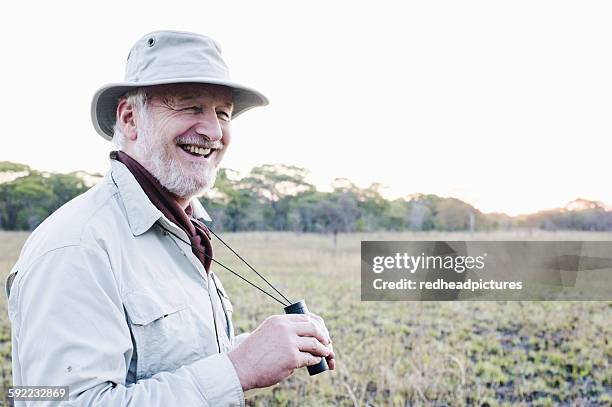 senior man holding binoculars on safari, kafue national park, zambia - safari park stock-fotos und bilder