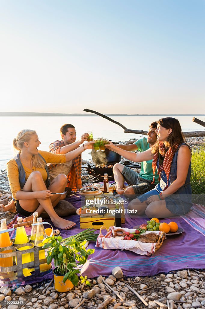 Friends sitting next to water having a picnic making a toast, Schondorf, Ammersee, Bavaria, Germany