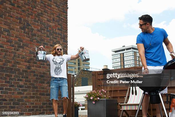 young man carrying ice buckets at rooftop barbecue - ice bucket stock-fotos und bilder