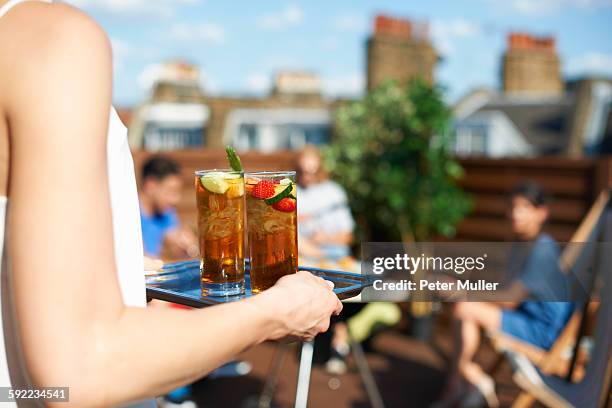 woman carrying tray of cocktails at rooftop party - plateau stockfoto's en -beelden