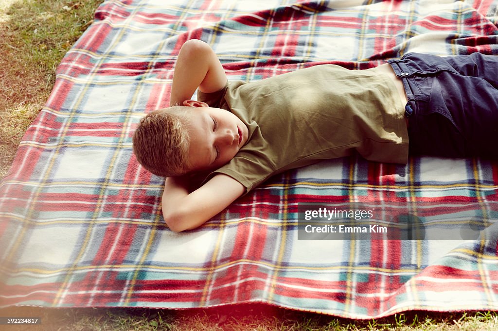 High angle view of boy lying on picnic blanket hands behind head looking away