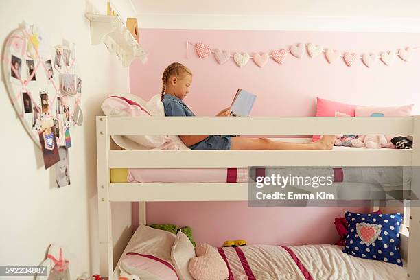 side view of girl sitting on top bunk of bunkbed reading magazine - kids in bunk bed stock pictures, royalty-free photos & images