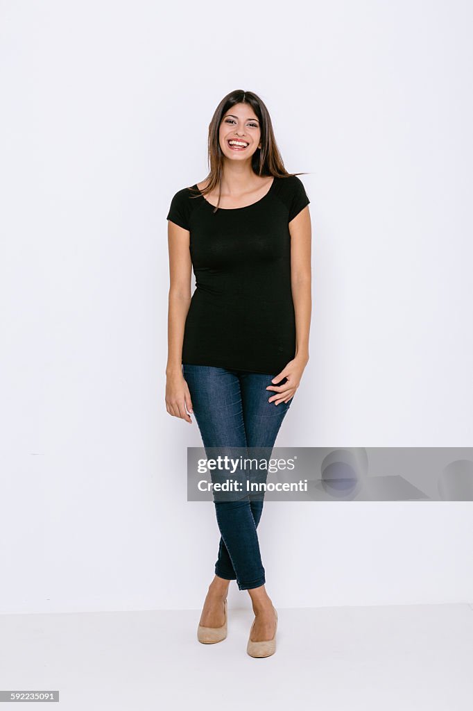 Full length front view of young woman standing legs crossed looking at camera smiling